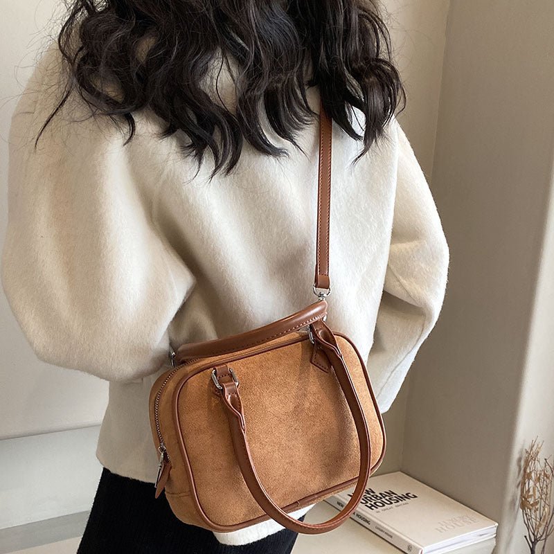 Brown suede crossbody bag with top handle, worn over shoulder with cream sweater