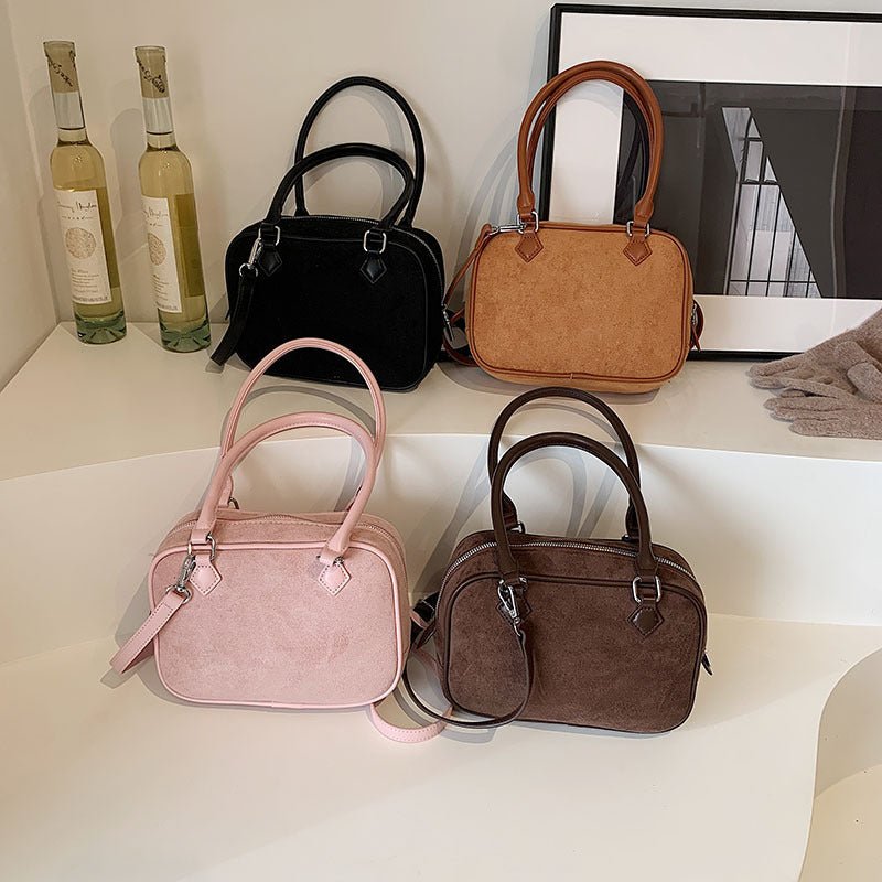 Suede handbags in pink, black, brown, and tan with top handles, displayed on white shelves with wine bottles.