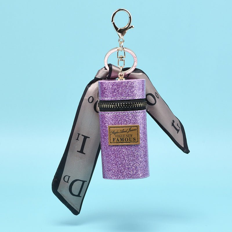 Glitter purple keychain pouch with ribbon, zipper, and 'Vogue New Famous' label, ideal for fashion accessories.