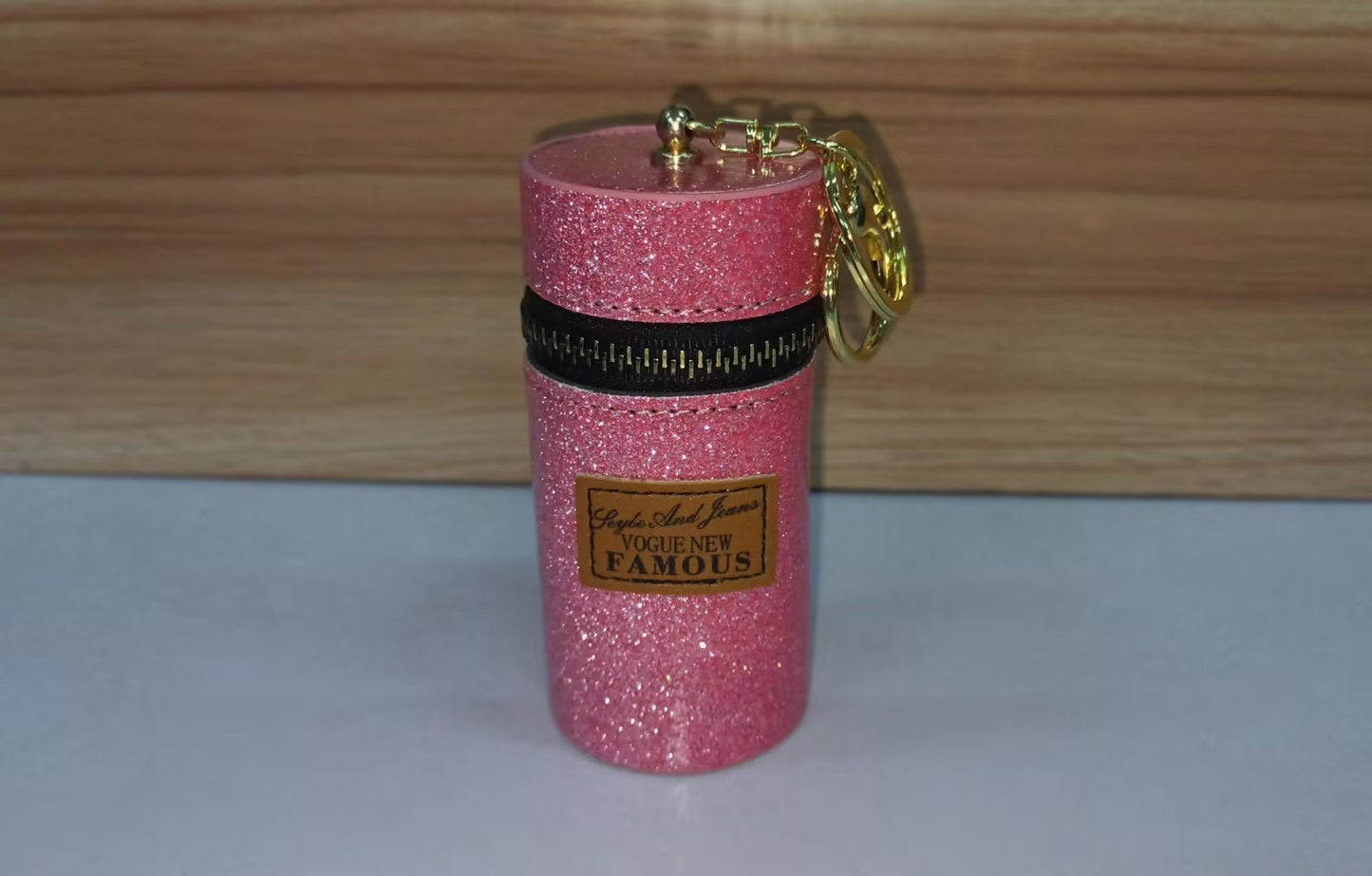 Pink glitter mini pouch with gold keychain, zip closure, and 'Vogue New Famous' label, ideal for small essentials.