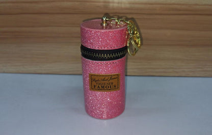 Pink glitter mini pouch with gold keychain, zip closure, and 'Vogue New Famous' label, ideal for small essentials.
