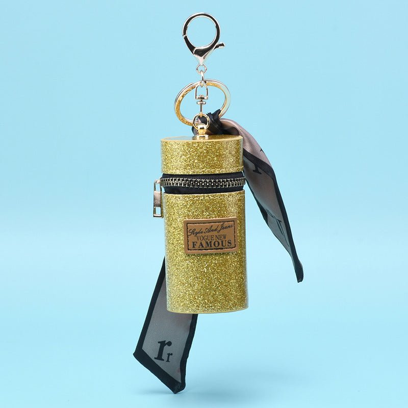 Glitter gold cylindrical keychain with black ribbon, zipper, and 'Vogue New Famous' label, perfect for fashion accessories.