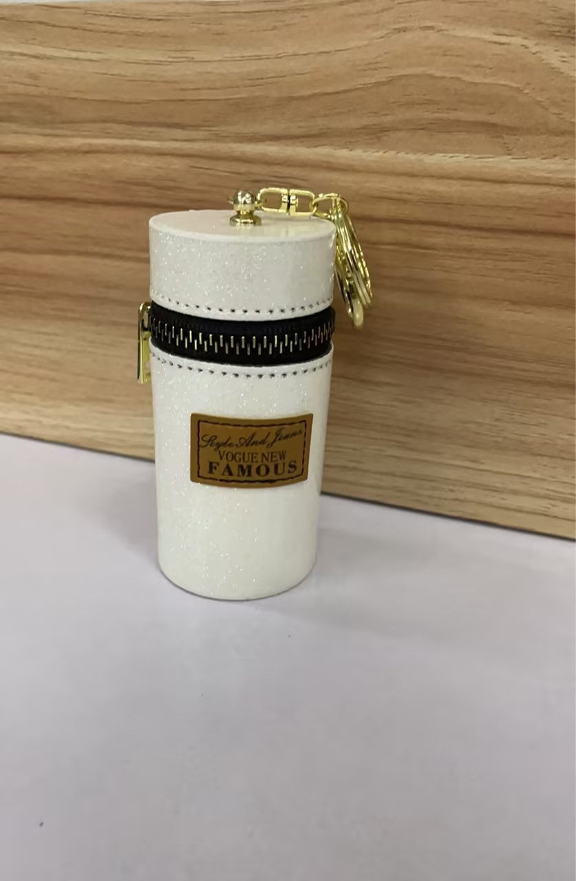 Glittery white cylindrical pouch with gold zipper, keychain, and 'Vogue New Famous' label, ideal for fashion accessories.