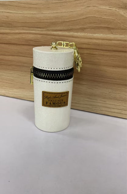 Glittery white cylindrical pouch with gold zipper, keychain, and 'Vogue New Famous' label, ideal for fashion accessories.