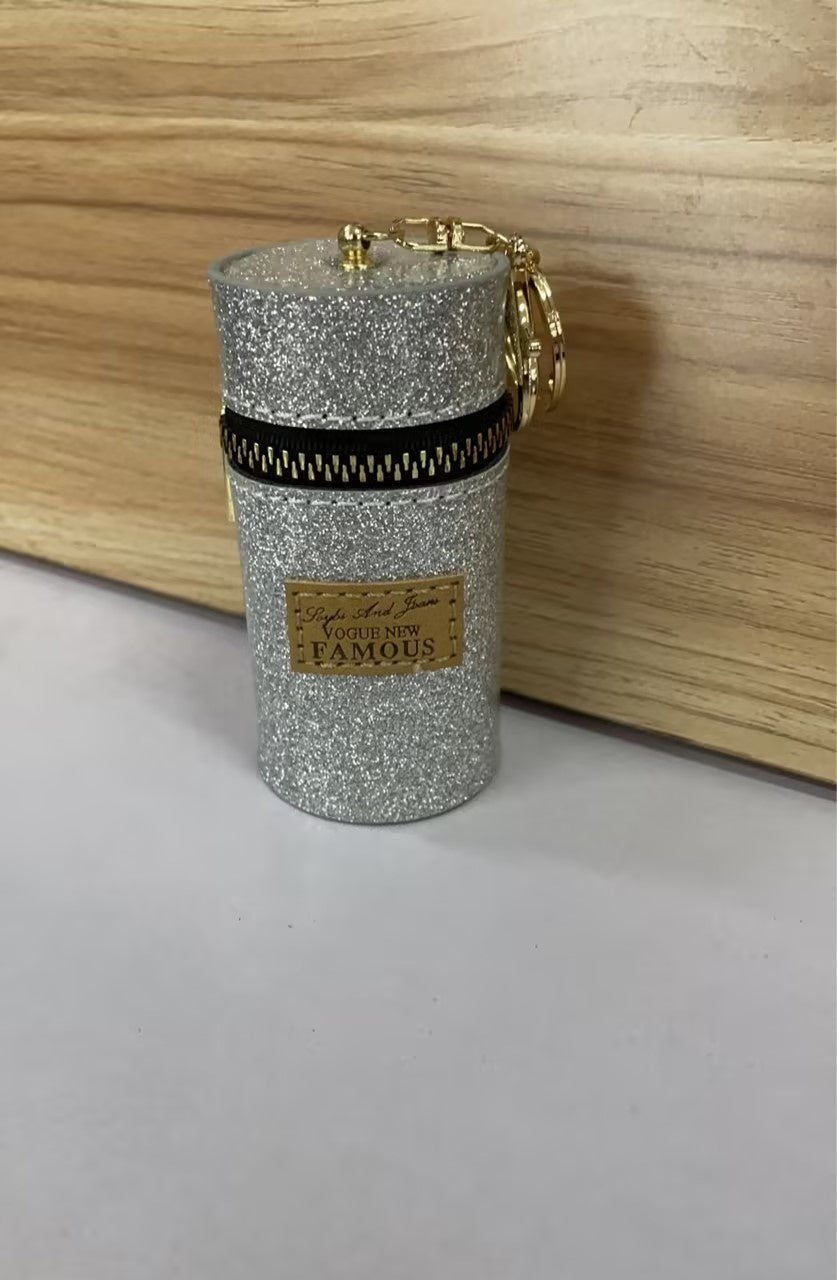 Glittery silver cylindrical keychain pouch with gold zipper and charm, labeled 'Vogue New Famous'
