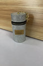 Glittery silver cylindrical keychain pouch with gold zipper and charm, labeled 'Vogue New Famous'