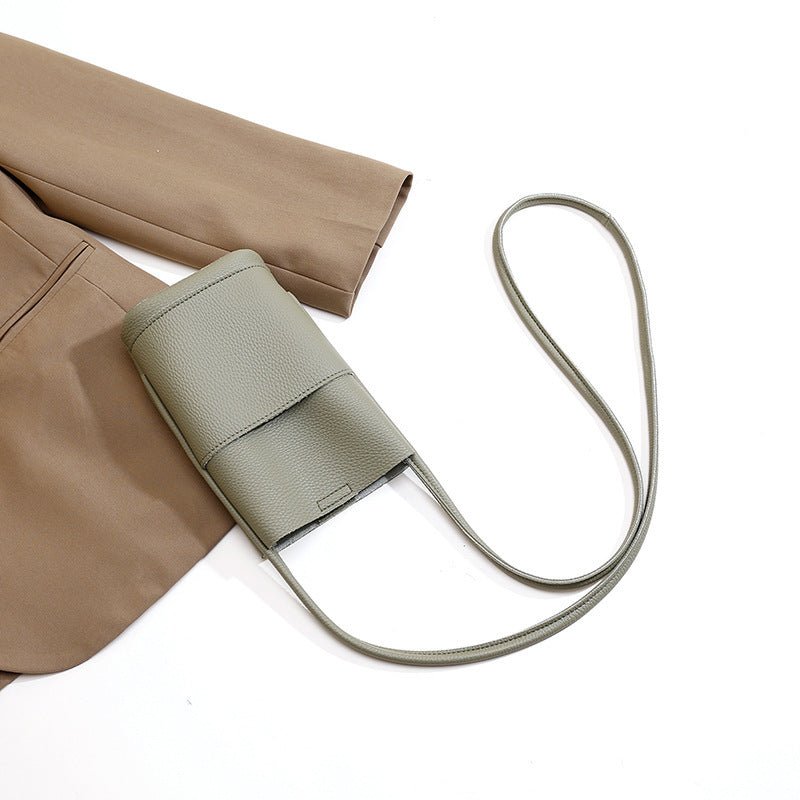 Sage green crossbody bag with textured leather and long strap, styled with beige pants