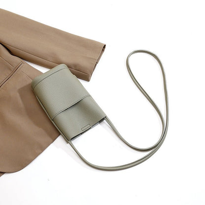 Sage green crossbody bag with textured leather and long strap, styled with beige pants