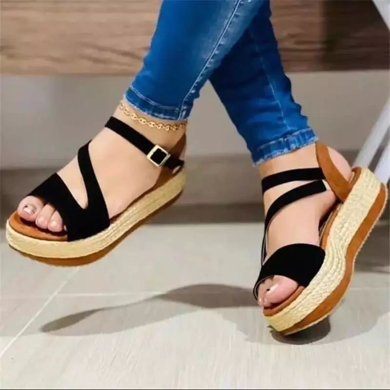 Black strappy espadrille wedge sandals with ankle buckle, worn with blue jeans for casual summer fashion.